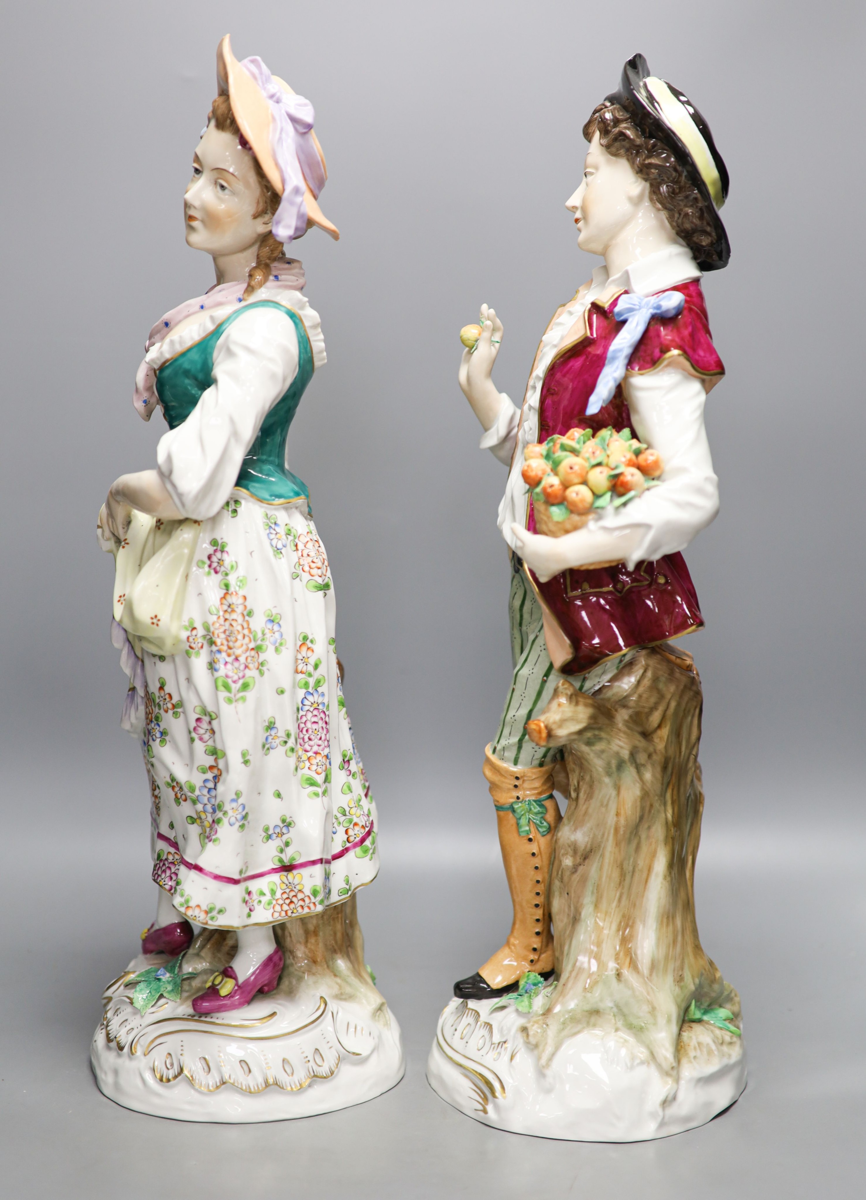 A pair of large Sitzendorf porcelain figures of a maid and a gallant, carrying baskets of fruit 52cm